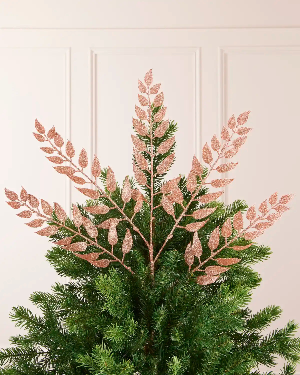 Rose Gold Leaf Christmas Tree Spray placed as a Christmas tree topper and a cream background. 