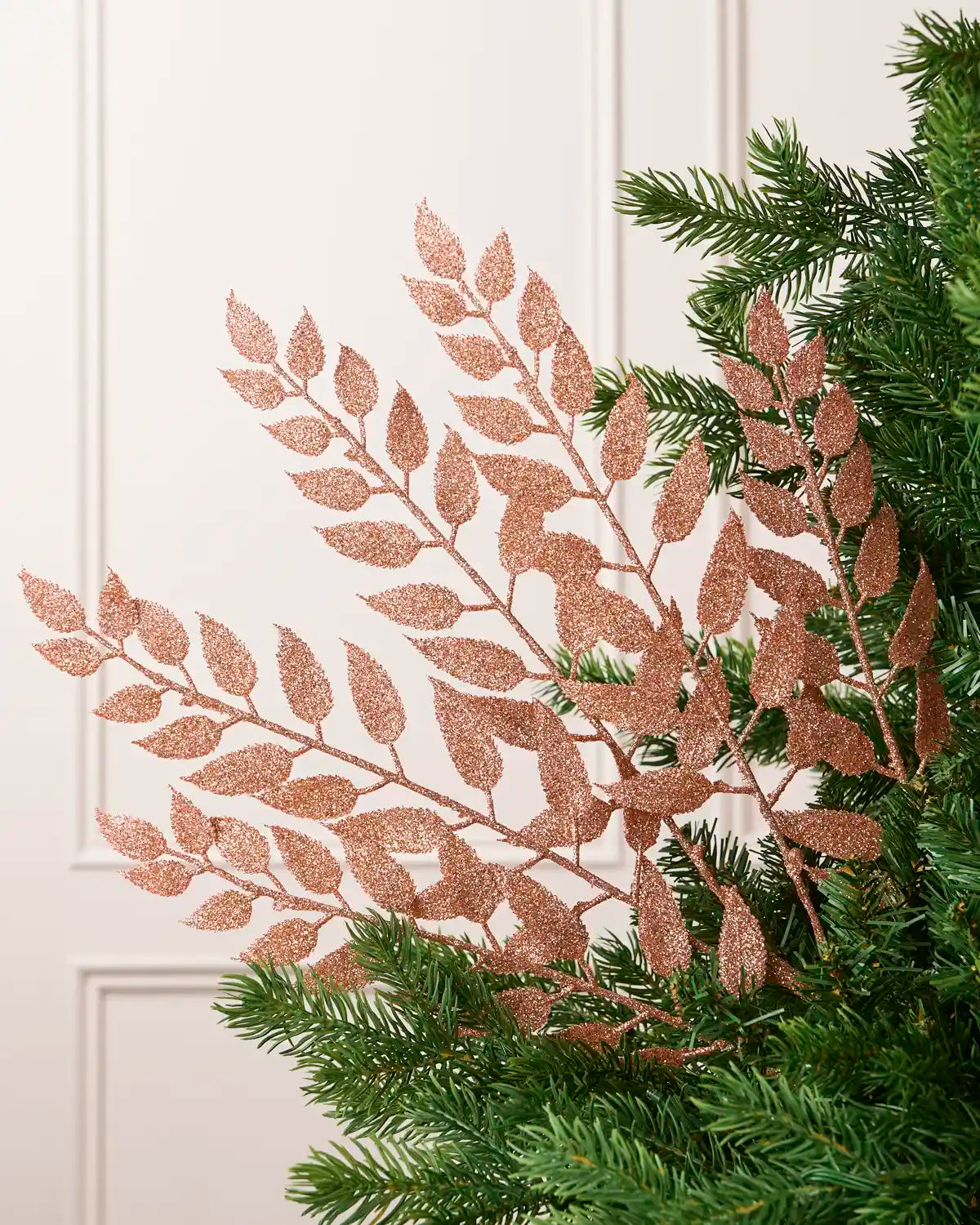 Rose Gold Leaf Christmas Tree Spray placed in Christmas tree branches with cream background