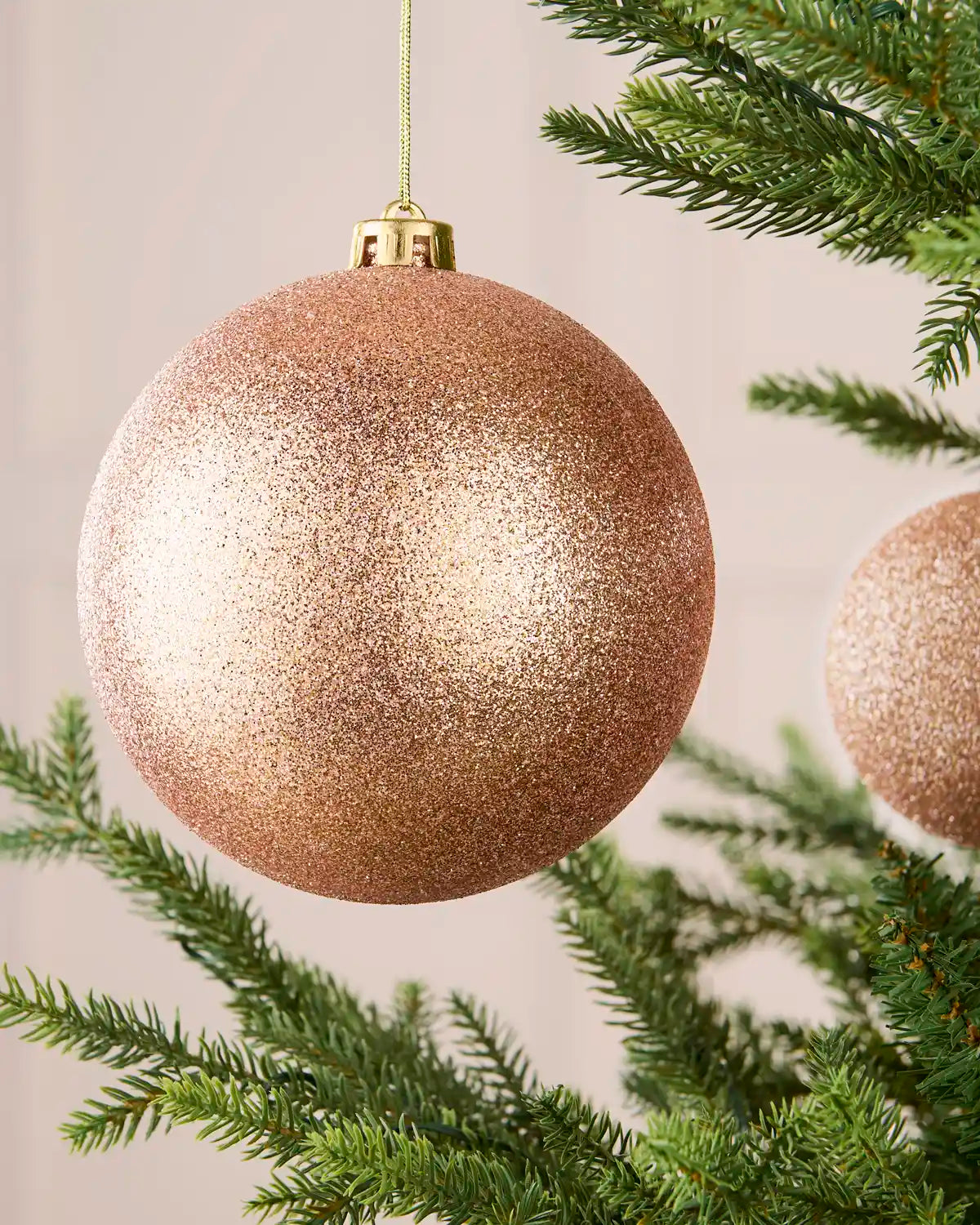 Close-up of a rose gold oversized glitter shatterproof bauble hanging on a Christmas tree, 15 cm