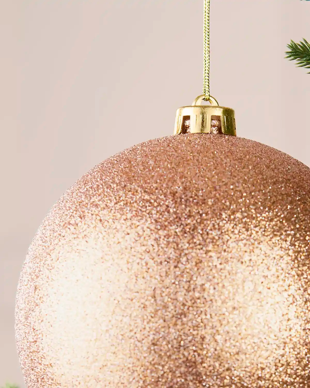 Detail view of a rose gold oversized glitter shatterproof bauble with gold cap and hanging string, 15 cm