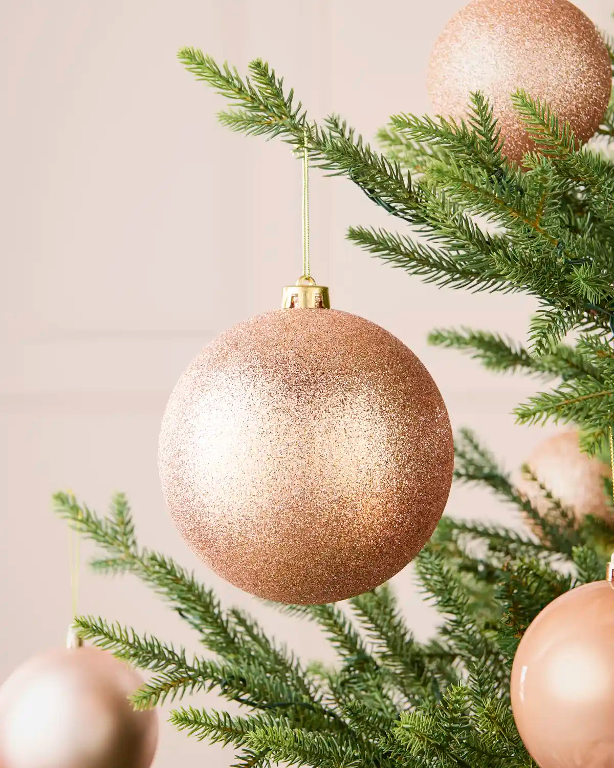 Rose gold oversized glitter shatterproof bauble on a Christmas tree with coordinating baubles, 15 cm