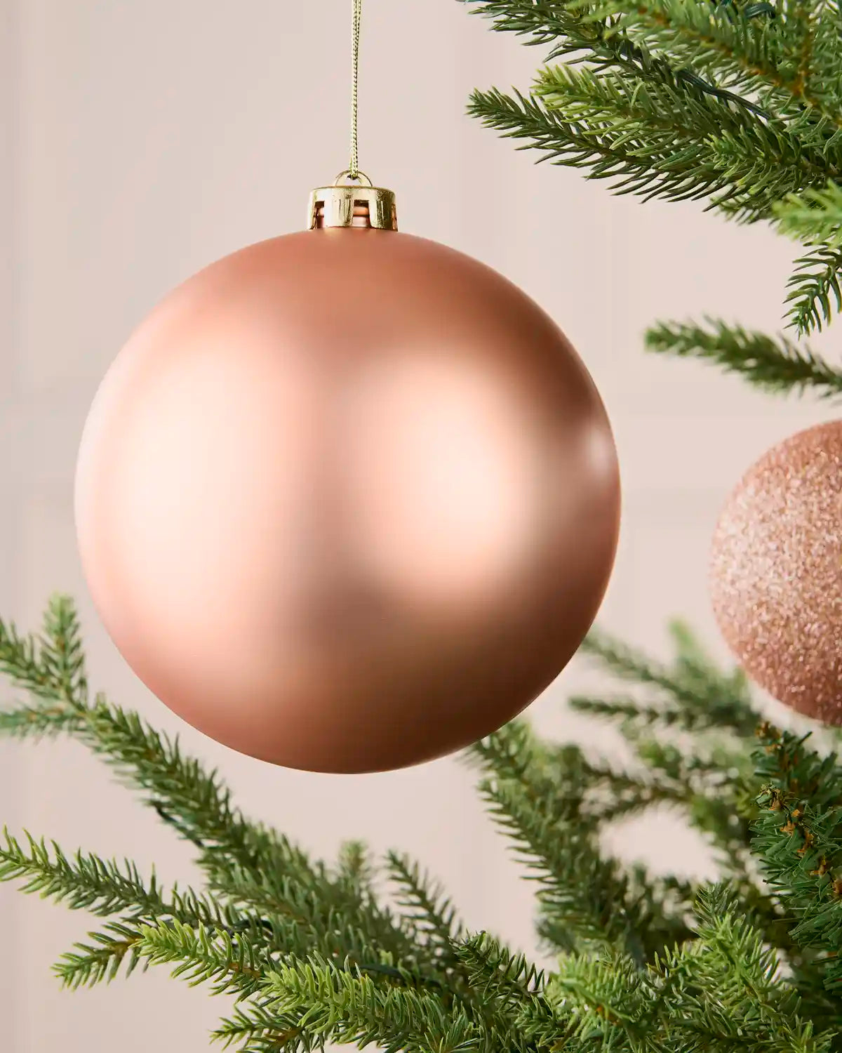 Close-up of a rose gold oversized matt shatterproof bauble hanging on a Christmas tree, 15 cm