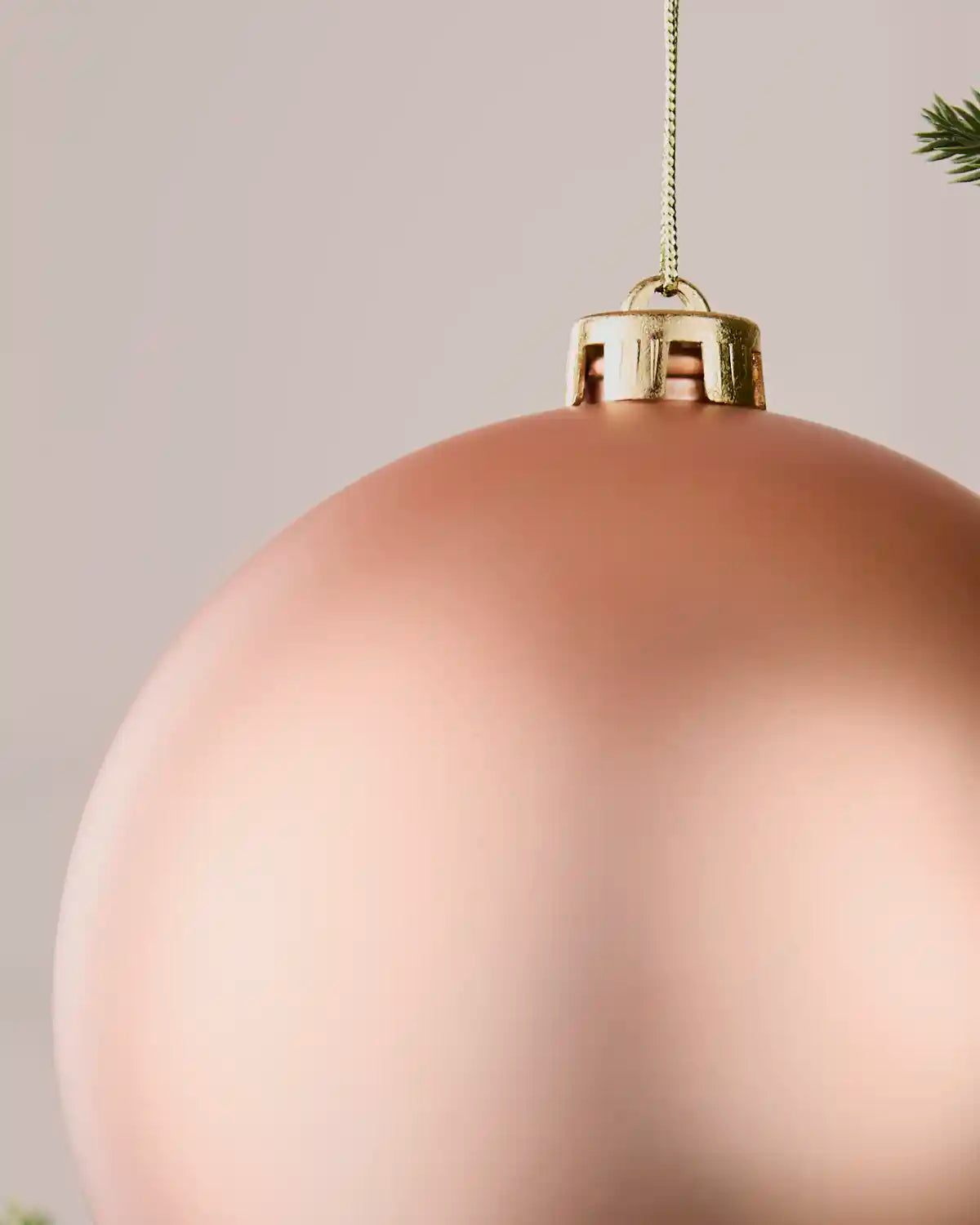 Detail view of a rose gold oversized matt shatterproof bauble with gold cap and hanging string, 15 cm