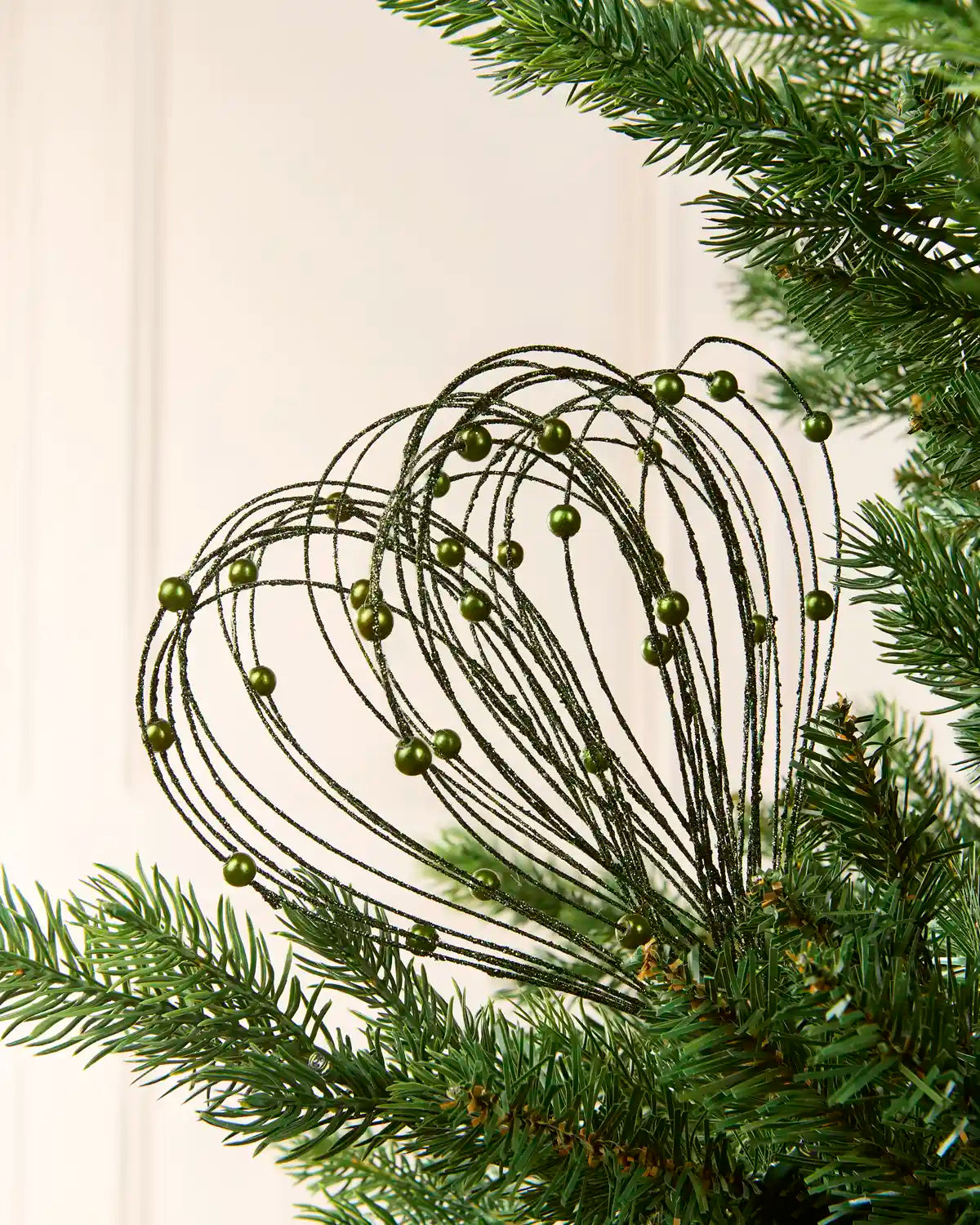 Sage Green Glitter Nest Christmas Tree Pick placed in green Christmas tree branches with a cream background
