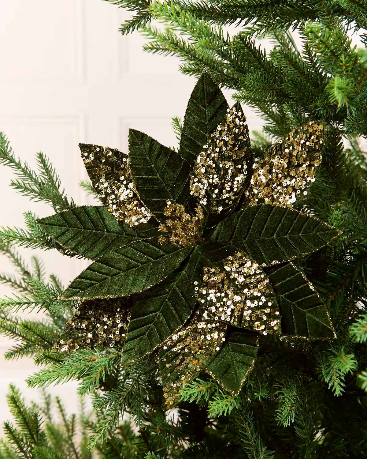 Sage Green & Gold glitter artificial poinsettia flower displayed on a Christmas tree, featuring layered pointed petals with gold glitter outlining the edges and veins and a sparkling gold center.
