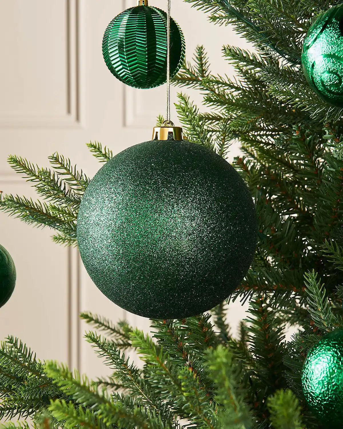 Sage glitter green oversized 15cm bauble on a Christmas tree branch with 4 smaller green baubles in the background