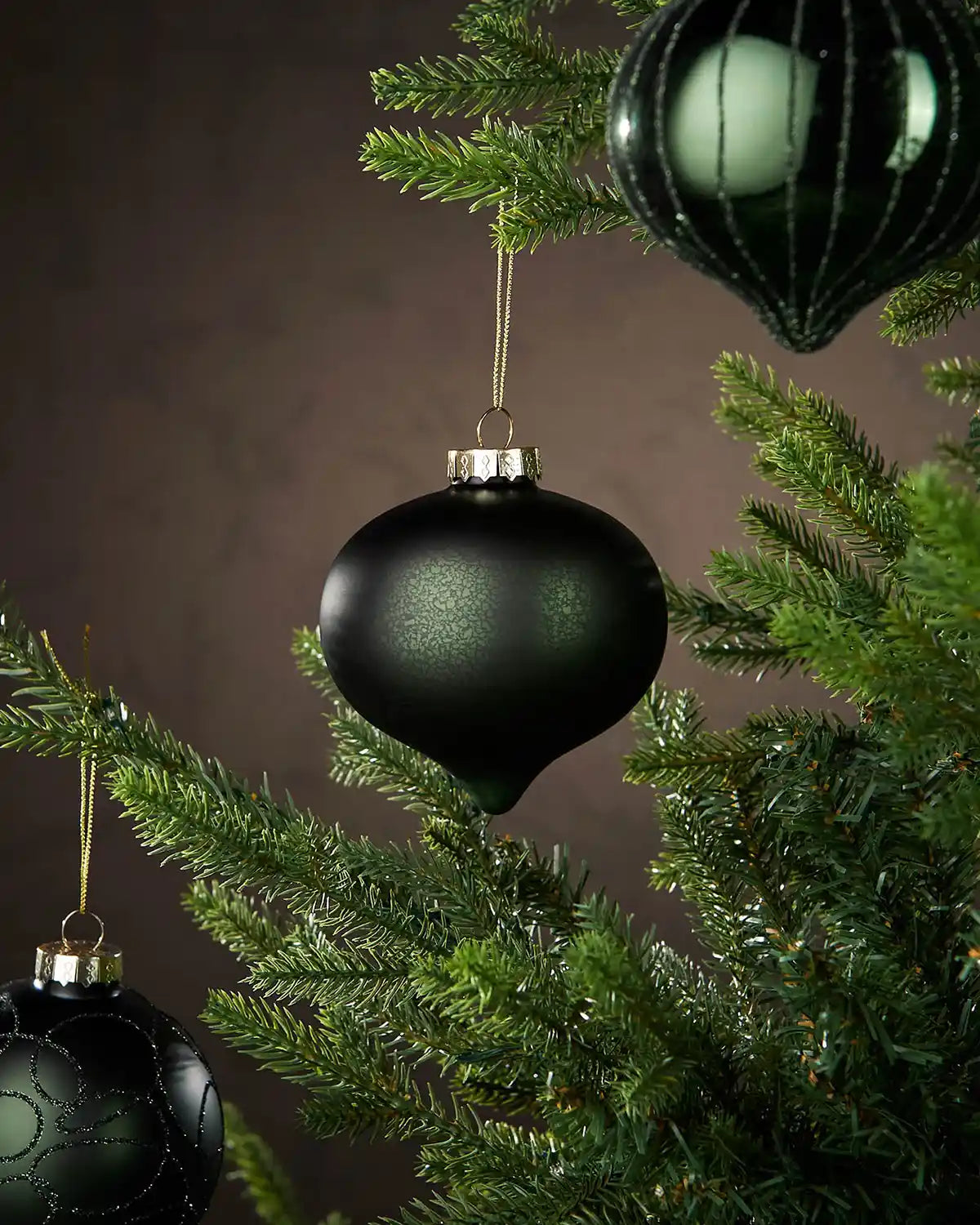 Sage green Christmas ornaments hanging on a tree with a dark background