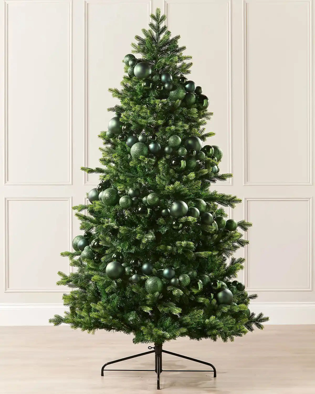 Sage green bauble garland wrapped around a Christmas tree against a cream panel wall and a wooden floor 
