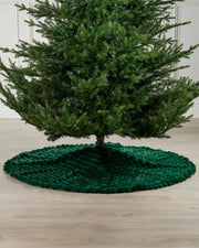 Sage green faux fur diamond tree skirt on light wooden flooring underneath green Christmas tree 