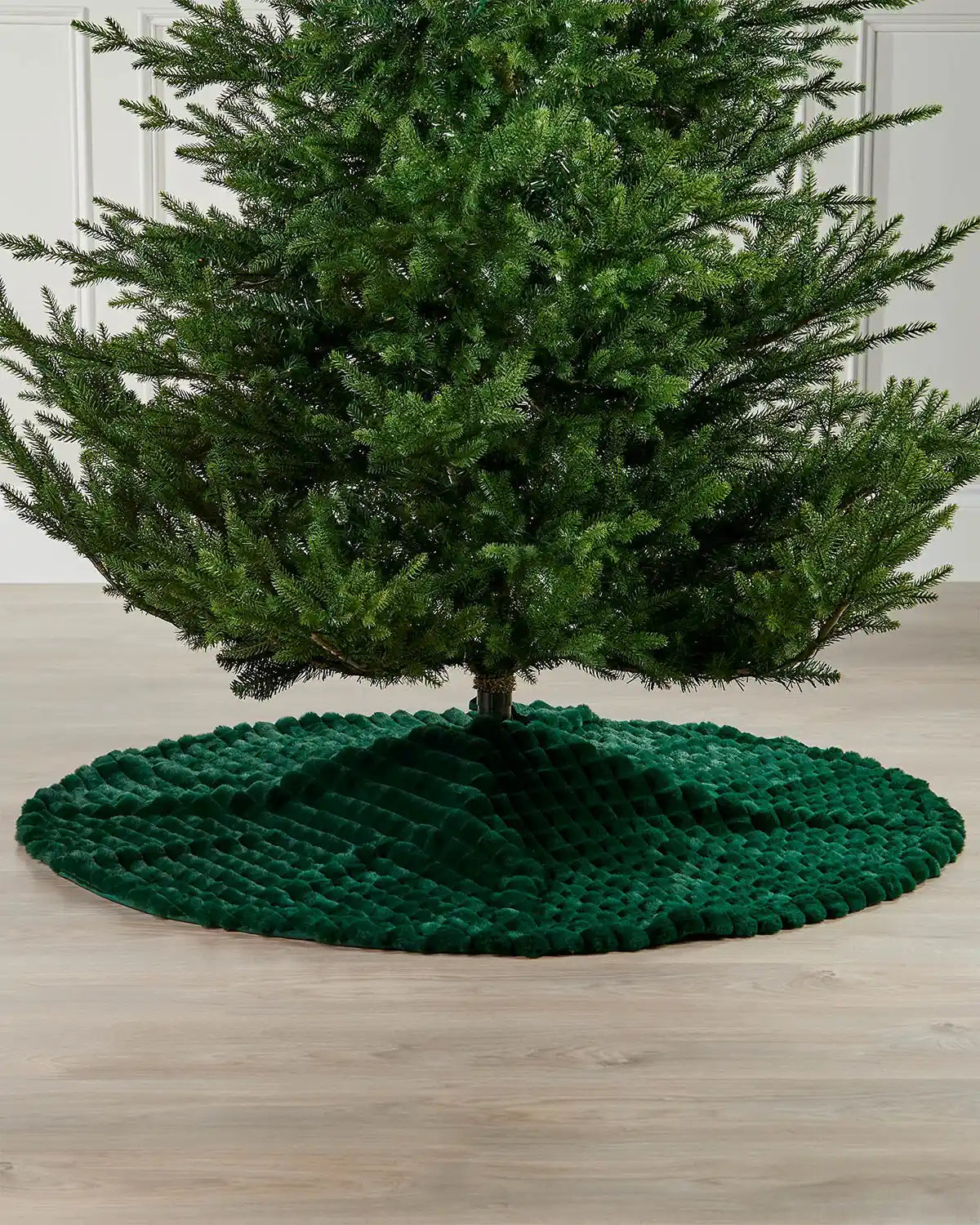 Sage green faux fur diamond tree skirt on light wooden flooring underneath green Christmas tree 