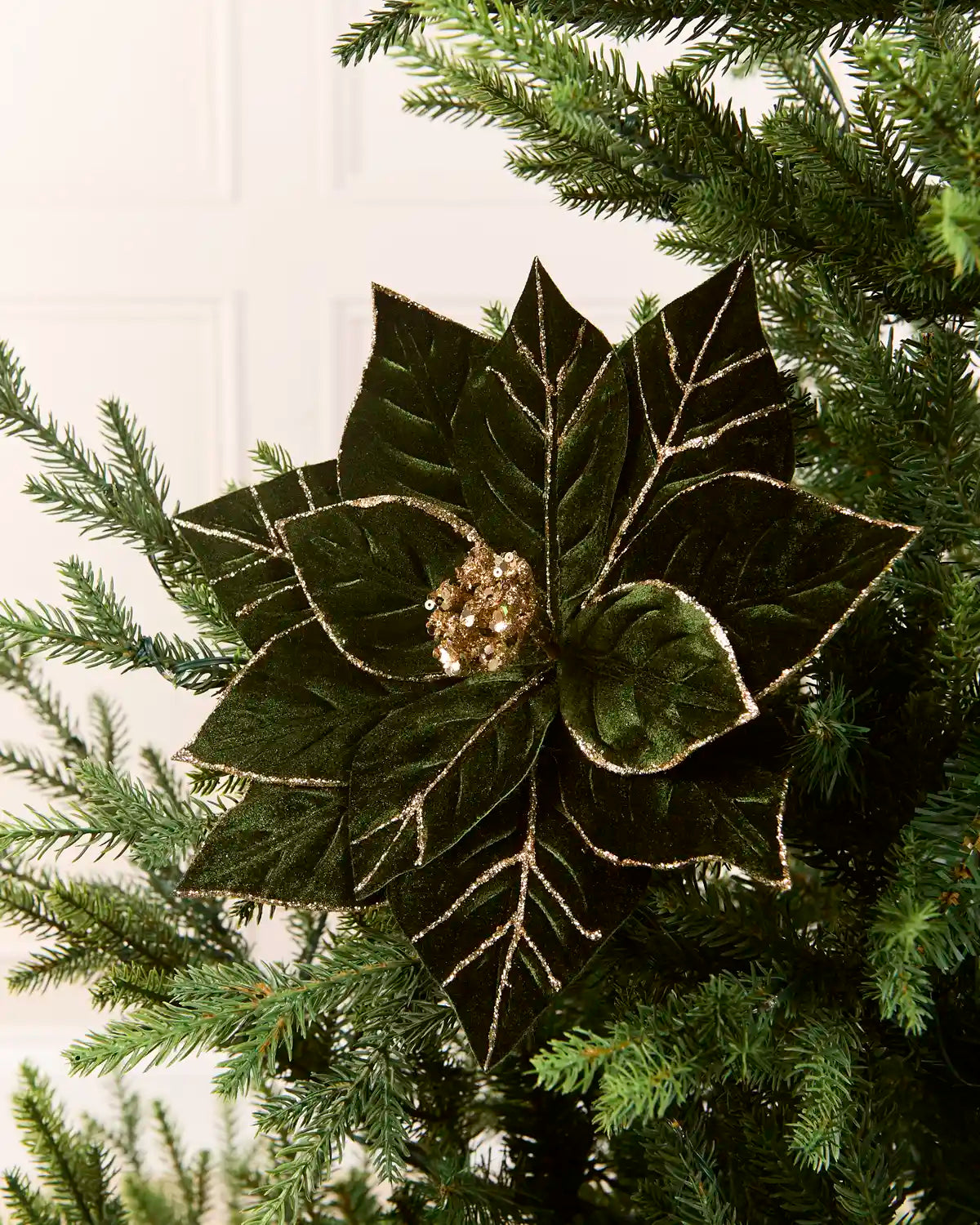 Sage green glitter artificial poinsettia flower displayed on a Christmas tree, featuring layered pointed petals with gold glitter outlining the edges