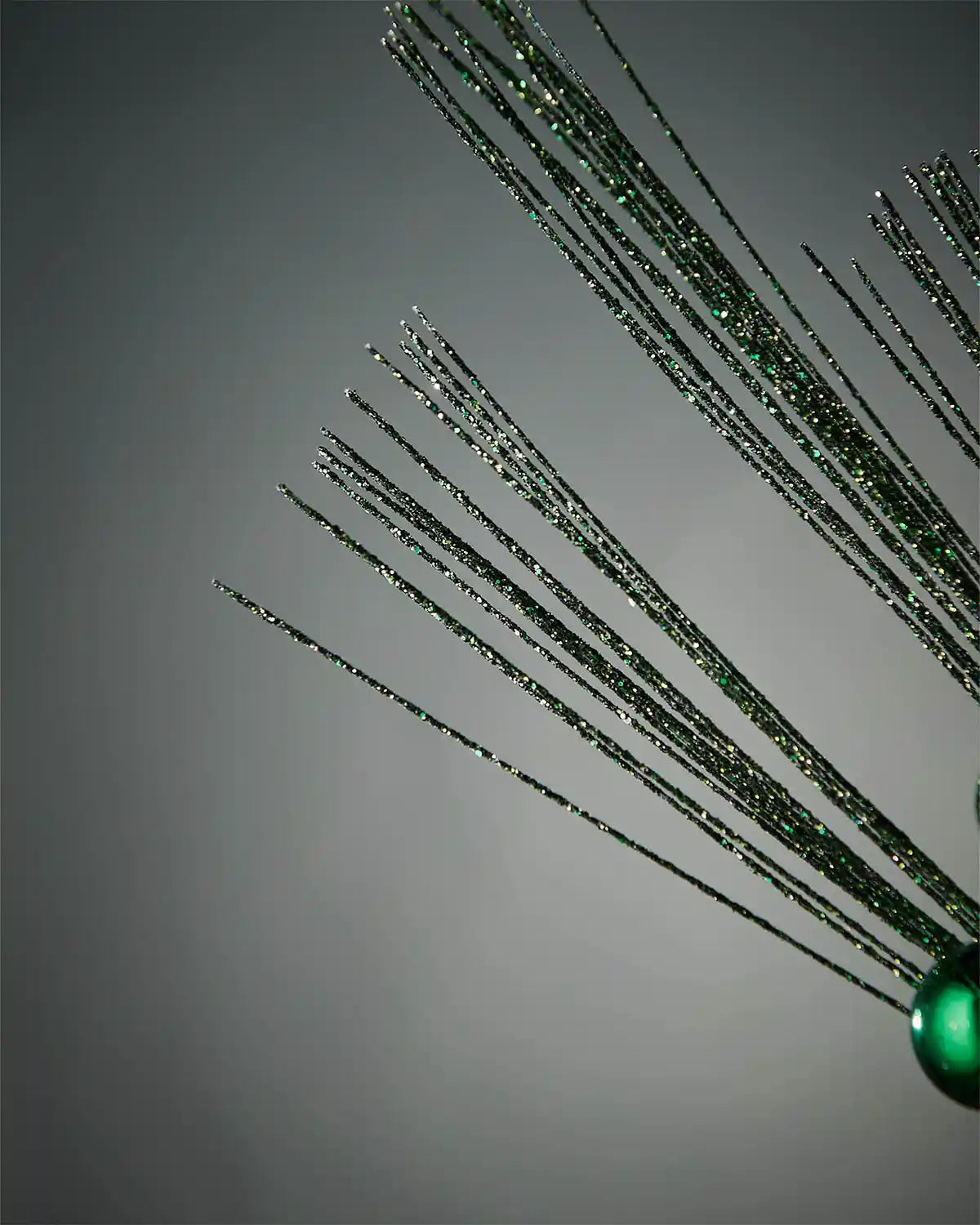 Close-up of foliage portion of sage green glitter bauble spray in front of grey wall