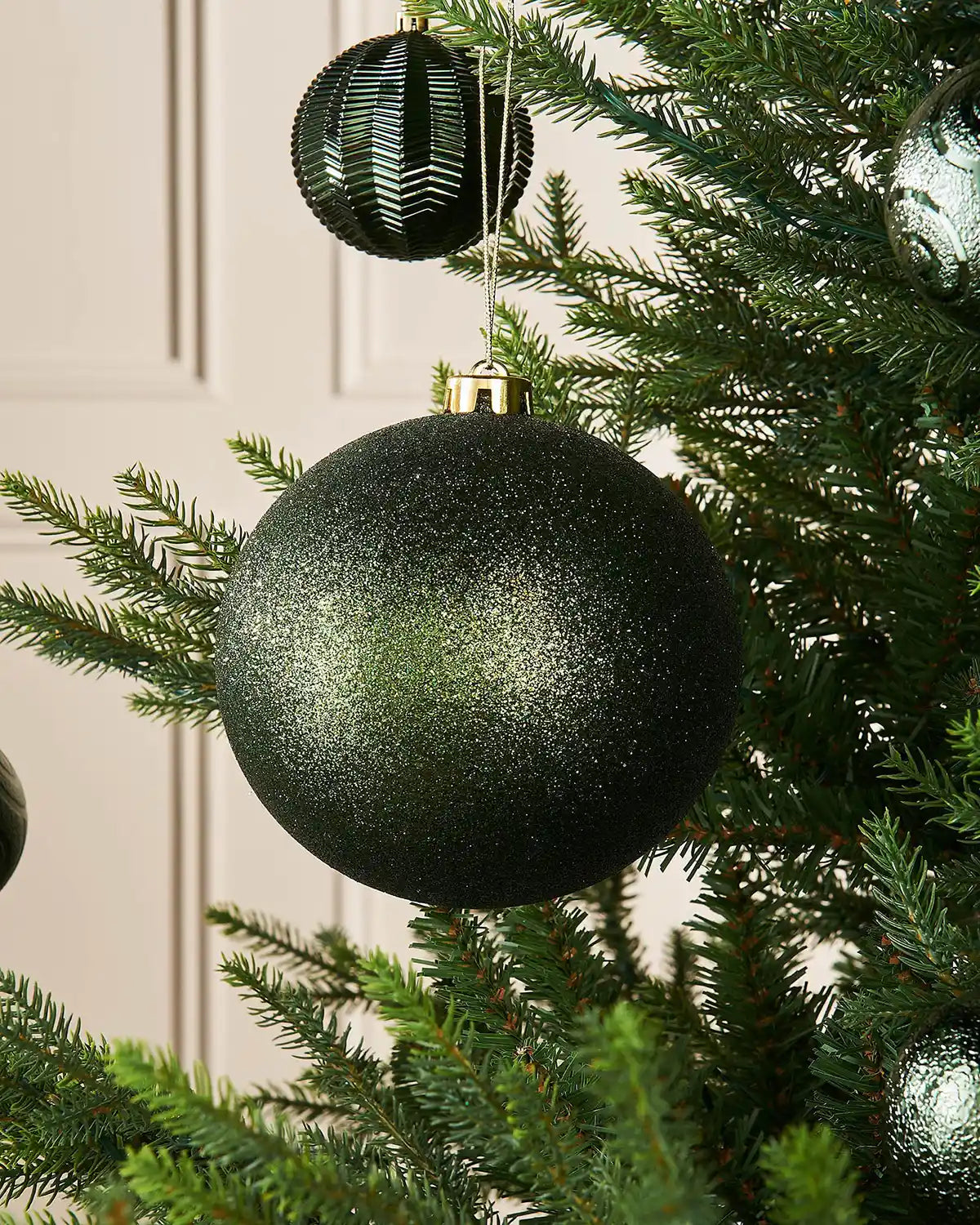 Sage green glitter oversized 15cm bauble on a Christmas tree branch with 4 smaller sage green baubles in the background