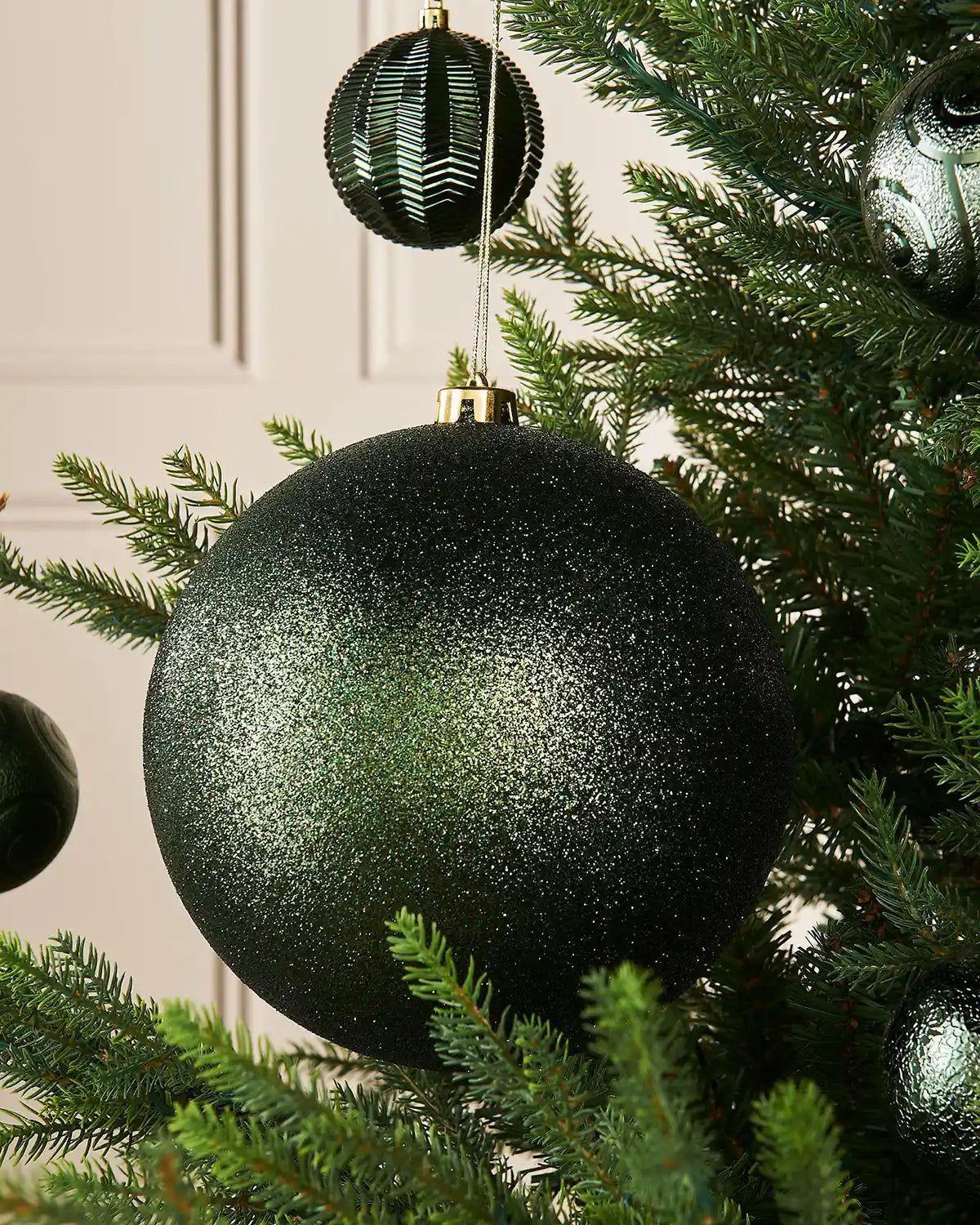 Sage green glitter oversized bauble on a Christmas tree branch with 4 smaller sage green baubles in the background