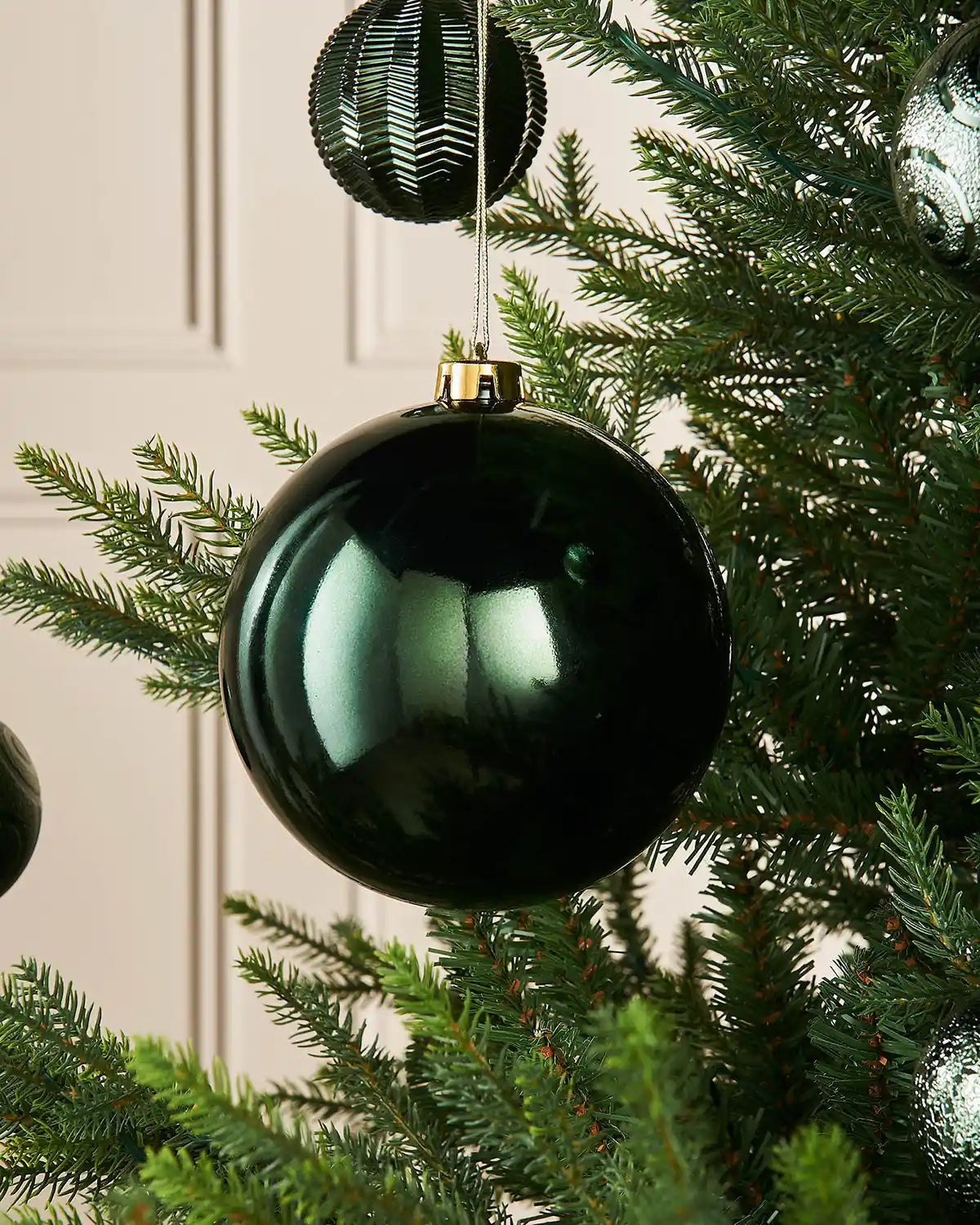 Sage green gloss oversized 15cm bauble on a Christmas tree branch with 4 smaller green baubles in background