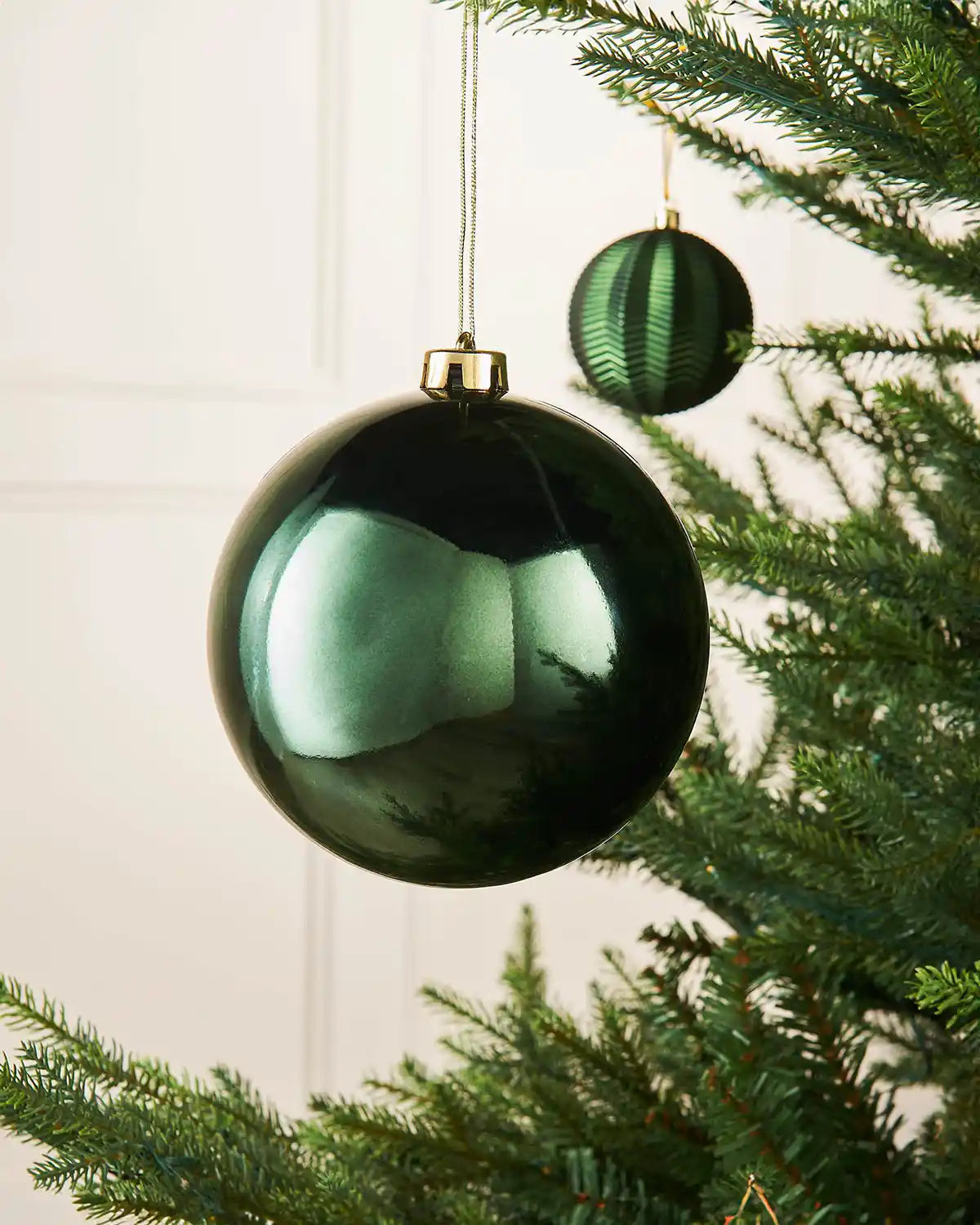 Sage green gloss oversized 15cm bauble on a Christmas tree branch with a smaller green bauble in background