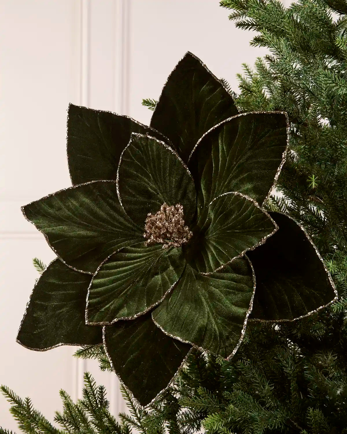 Sage green oversized velvet artificial poinsettia displayed on a Christmas tree, featuring layered velvet petals with glittered edges and a sparkling gold center
