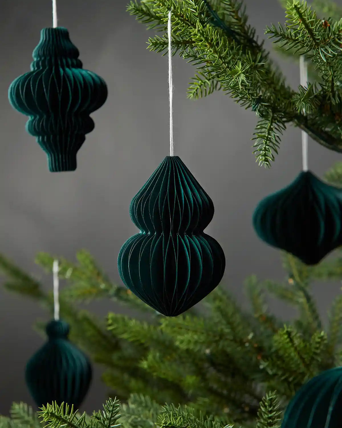 Image of scattered 10cm sage green paper honeycomb tree decorations hanging on Christmas tree in front of grey wall background