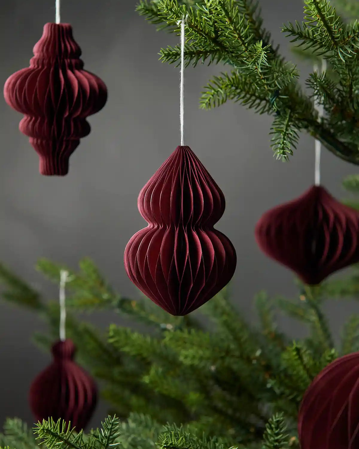 Image of scattered burgundy red paper hanging tree decorations on Christmas tree in front of grey wall background