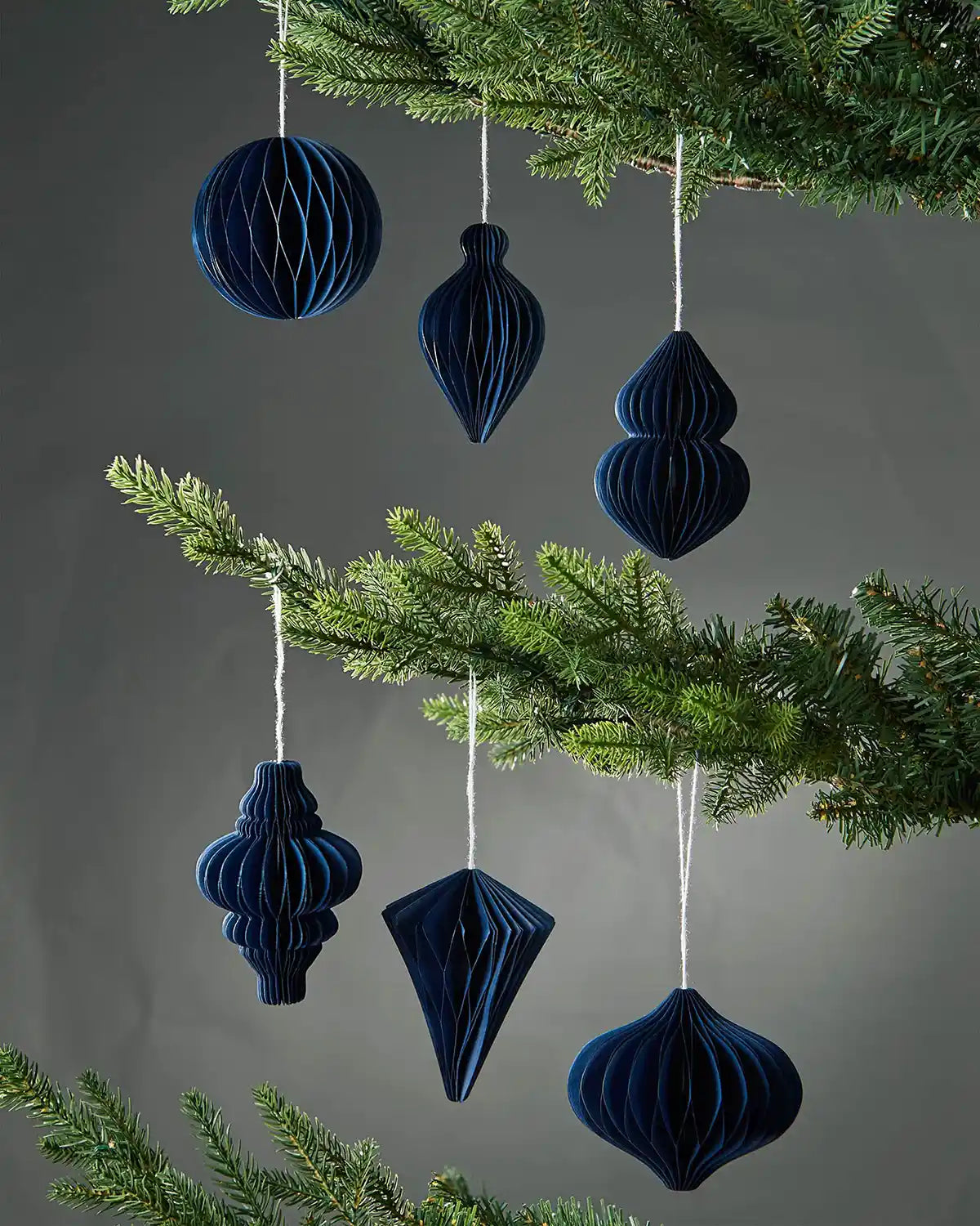 Set of 6 10cm navy blue honeycomb paper Christmas tree decorations hanging on a tree in front of grey wall background