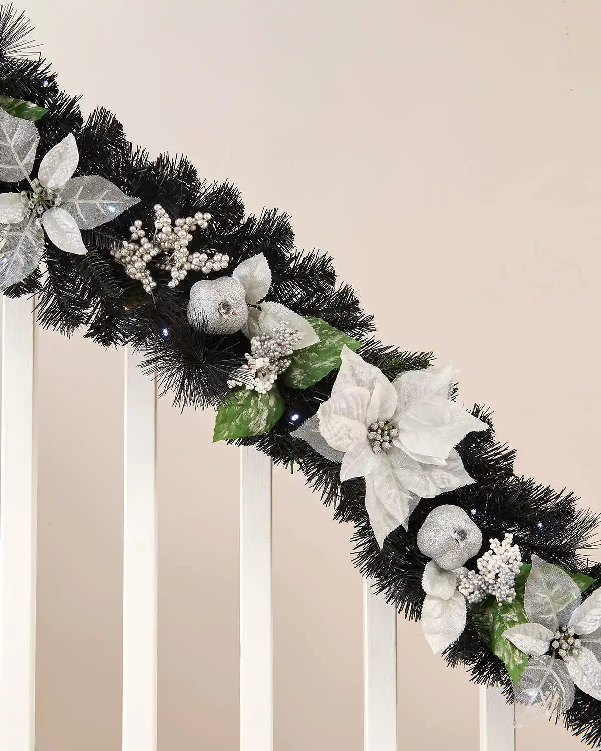 Semi-close image of black garland with bright white lighting and silver and white foliage on white wooden banister
