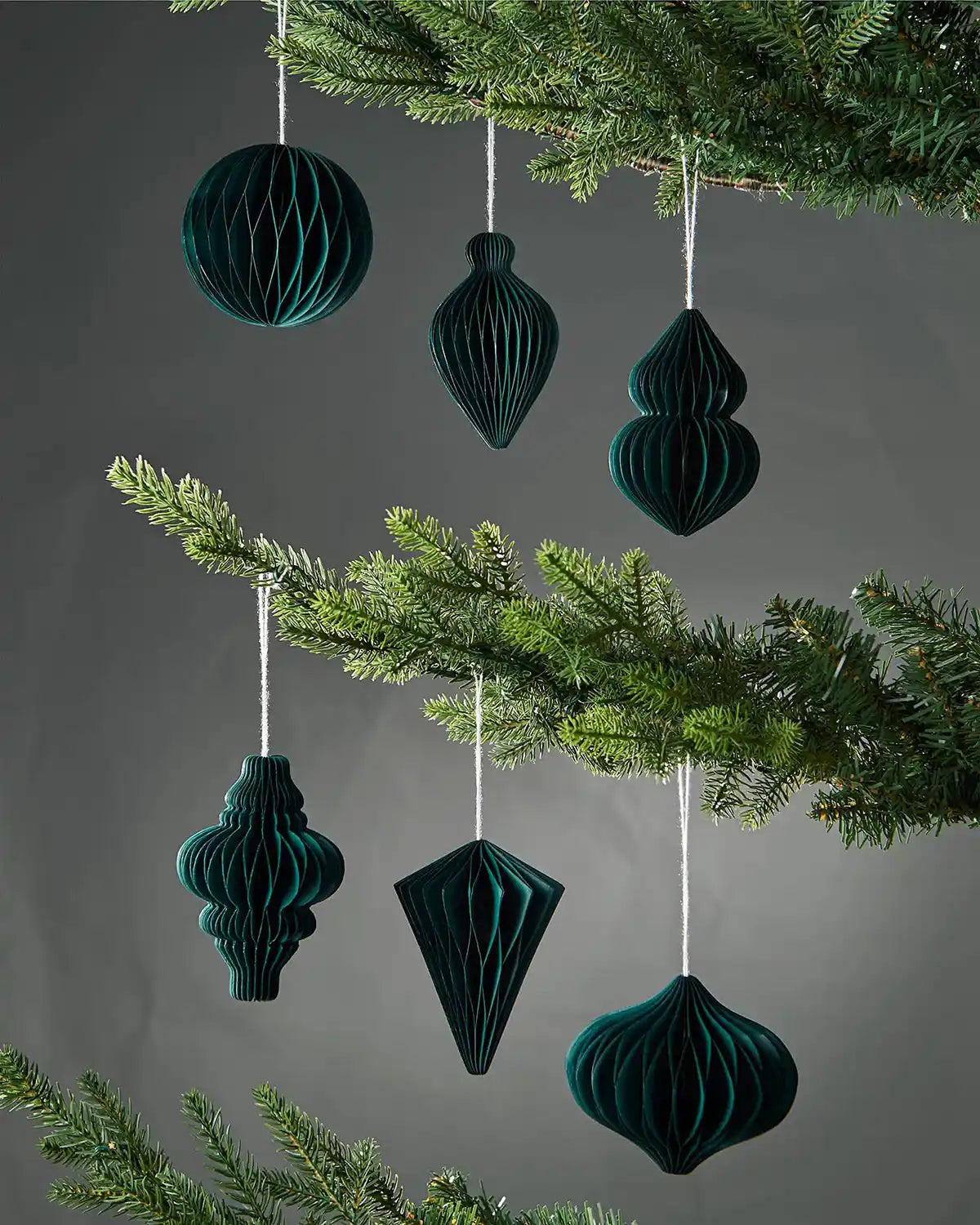 Set of 6 10cm sage green paper honeycomb tree decorations hanging on Christmas tree in front of grey wall background