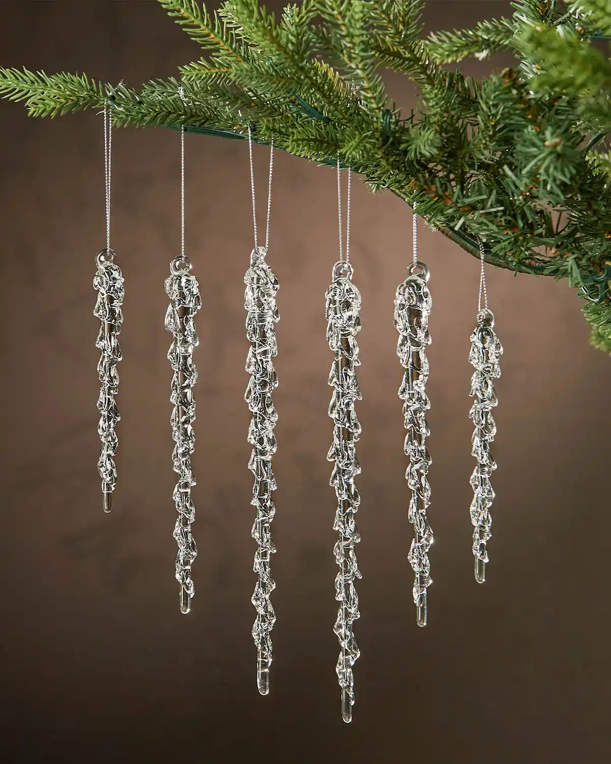 Set of 6 melting Icicle ornaments hanging on a Christmas tree with a brown background