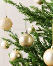 Seven Latte Christmas tree ornaments hanging from green pine branches against a soft light background.
