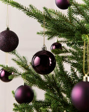 Seven Purple baubles on a Gold string hanging off a Christmas Tree against a cream background