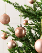 Seven Rose Gold Baubles hanging from a Christmas tree against a cream background