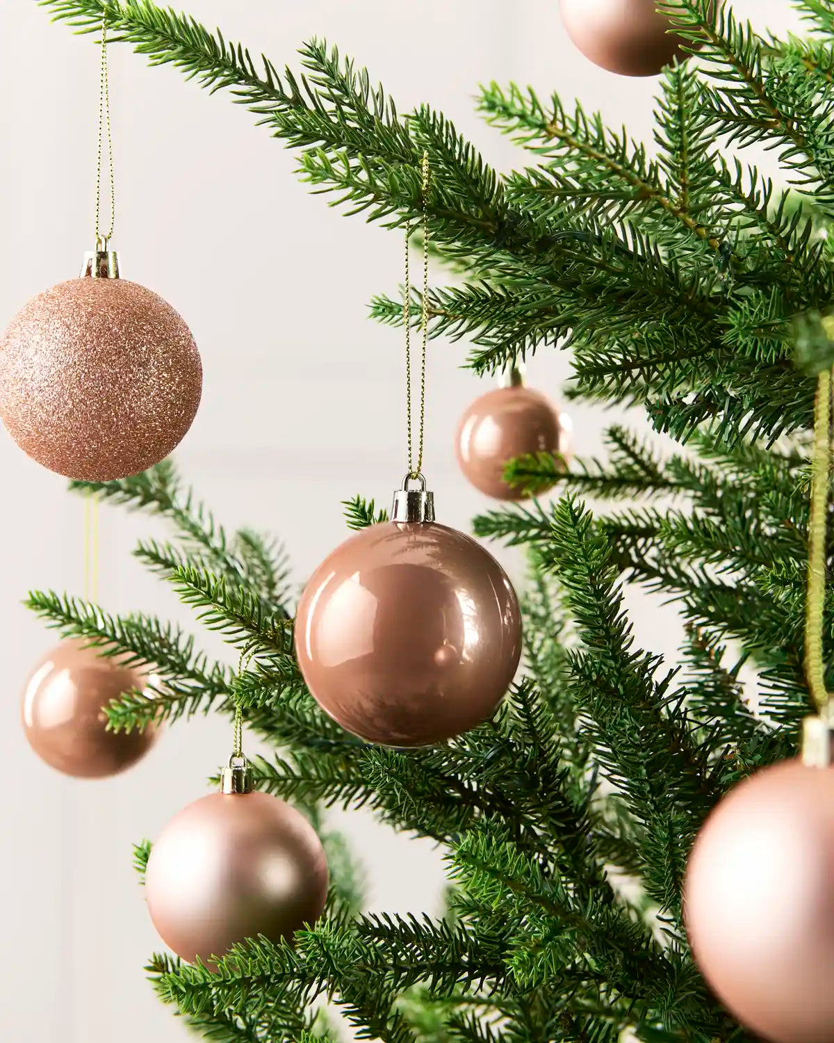 Seven Rose Gold Baubles hanging from a Christmas tree against a cream background