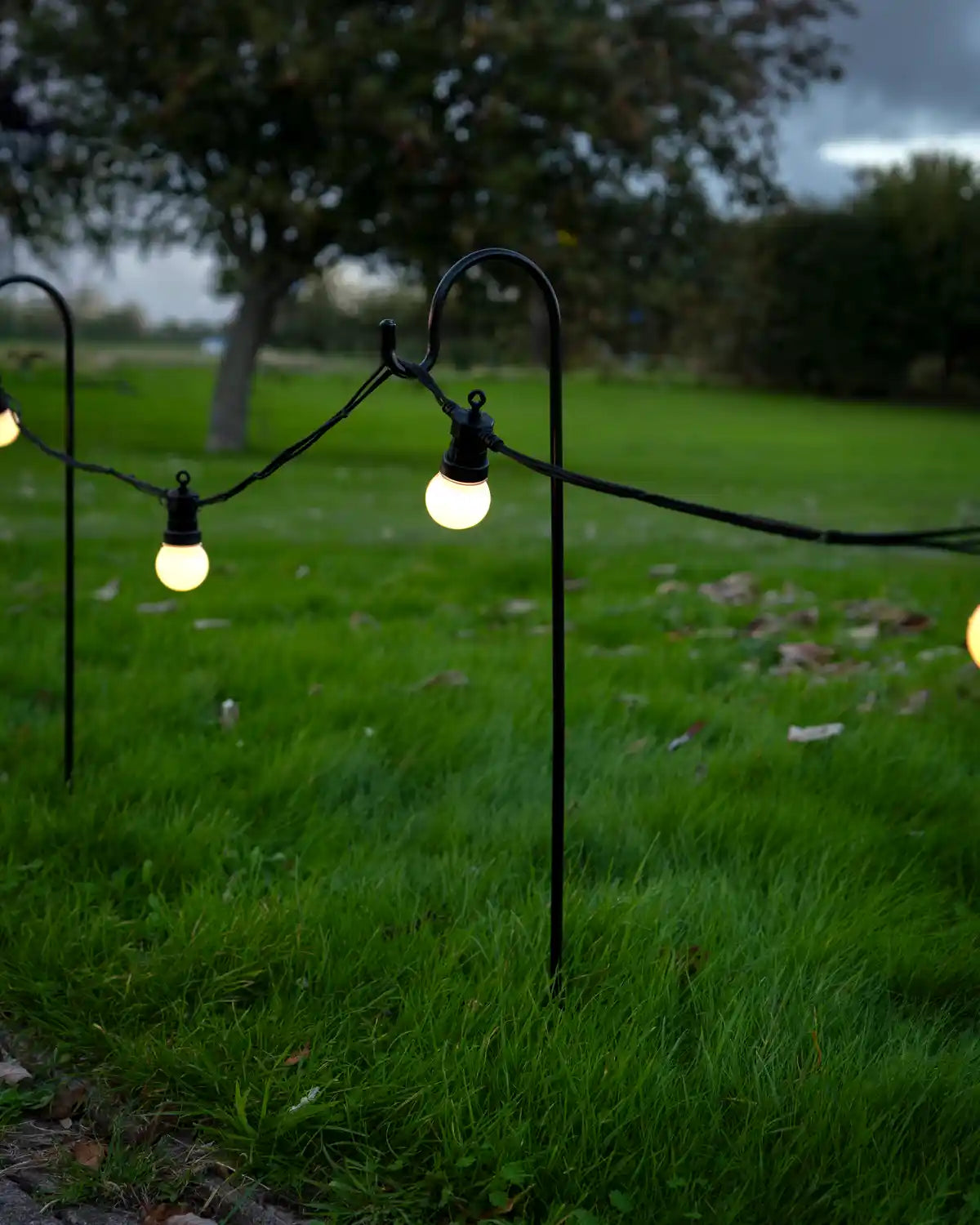 Shepherd’s hook garden stake with a curved black metal top supporting outdoor string lights