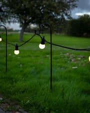 Shepherd’s hook garden stake with a curved black metal top supporting outdoor string lights