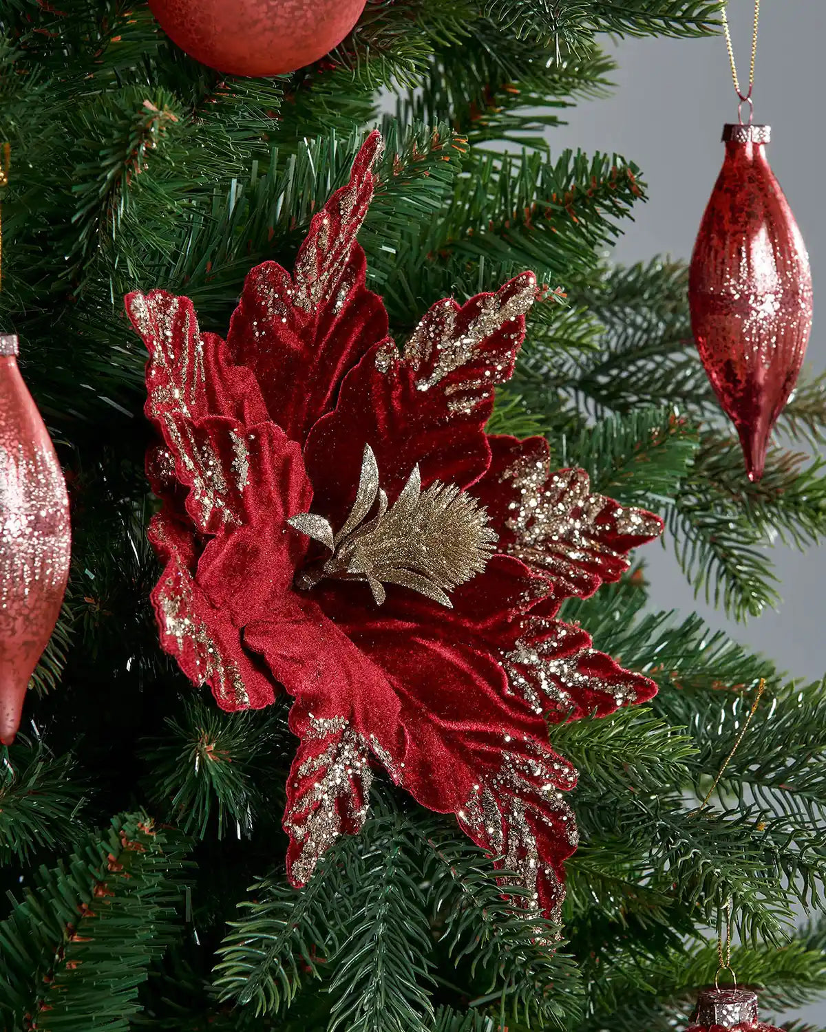 Side shot of Red and gold poinsettia flower with gold accents on a Christmas tree