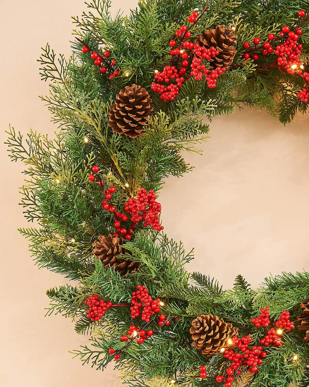 Side view Christmas wreath with greenery, red berries, and pinecones on a light background