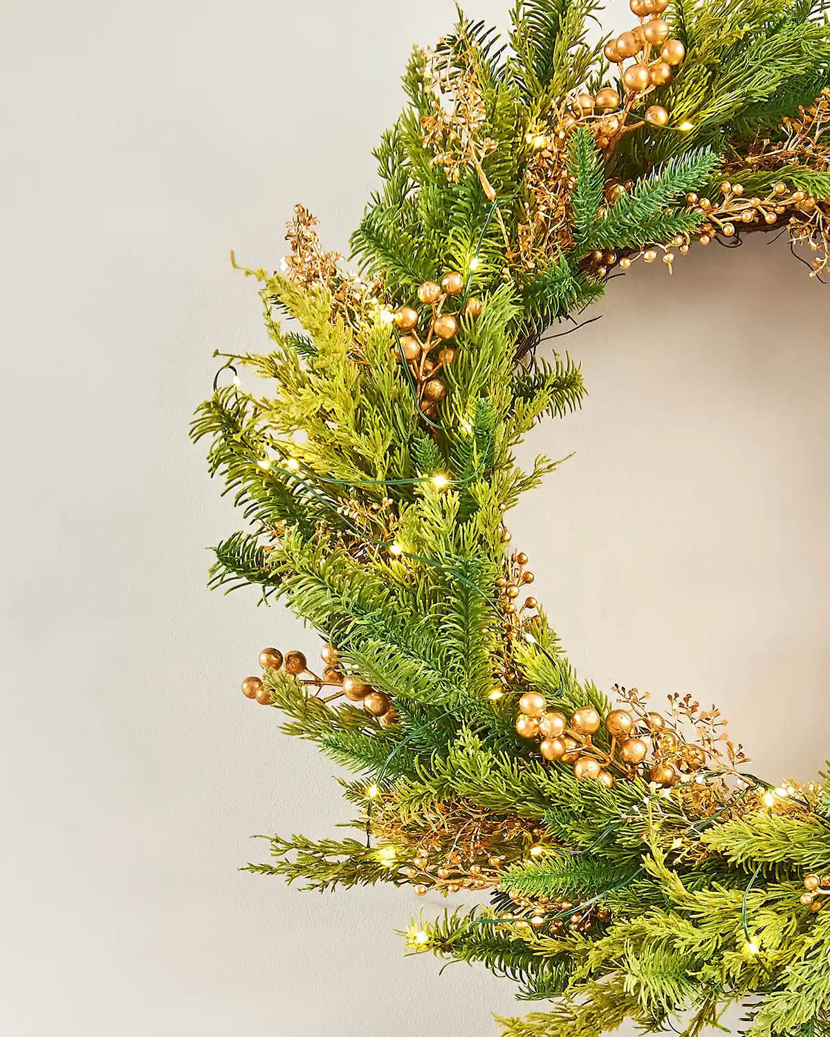 Side view Decorative Gold Berry wreath with greenery and small lights on a white background