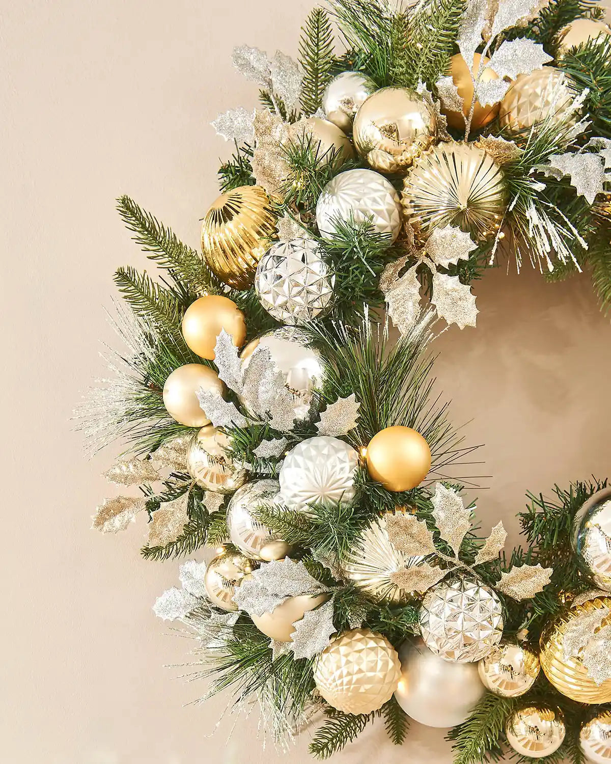 Side view of Decorative Christmas wreath with gold, silver, and white ornaments on a beige background