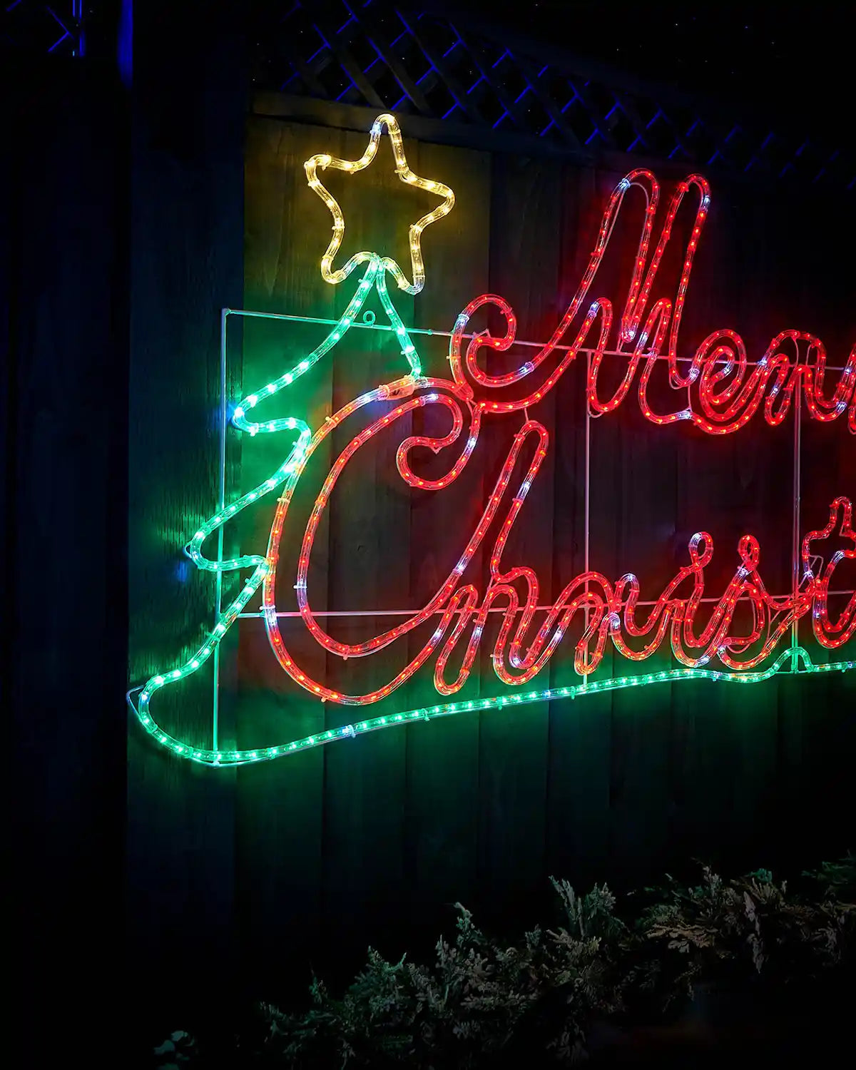 Side view of Red, green and yellow LED Merry Christmas Silhouette sign on a garden fence in a snowy garden  under a starry night sky
