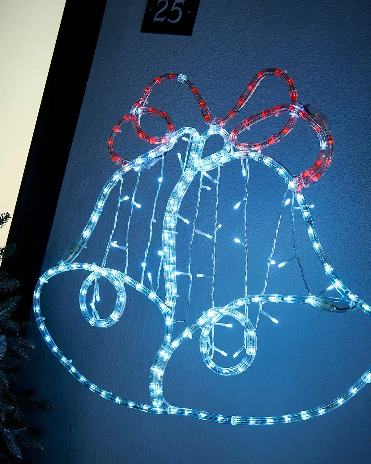 Side view of a White and Red Light up Christmas bell silhouette on a light coloured wall outside
