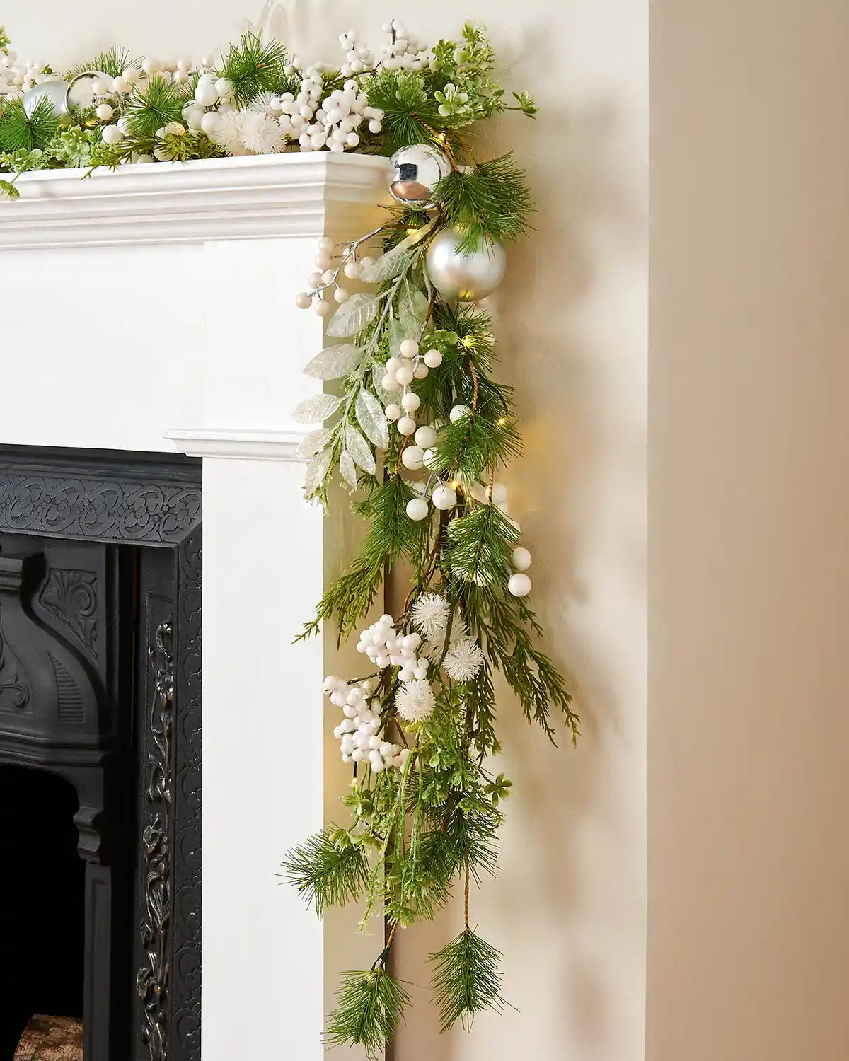 Side view of a decorative Christmas garland with white ornaments and lights on a fireplace mantel.