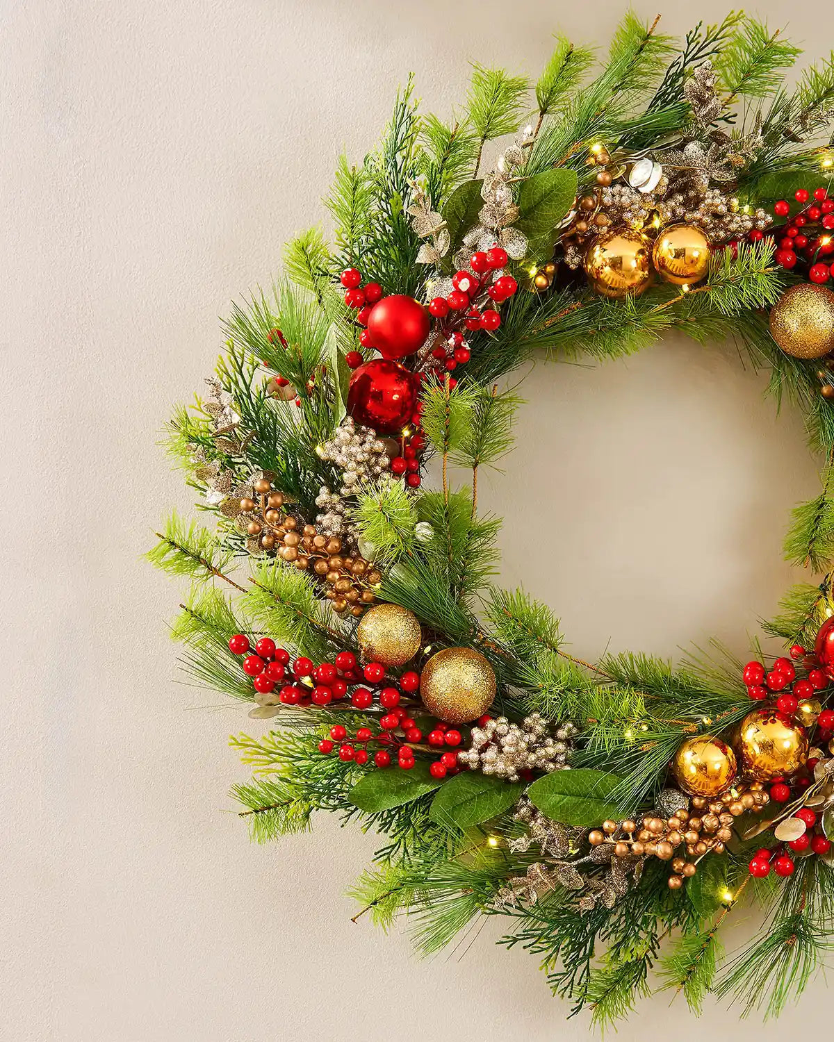 Side view of a decorative Christmas wreath with greenery, red berries, and gold ornaments on a cream background