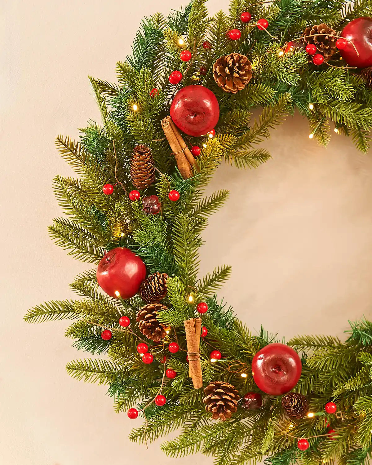 Side view of decorated wreath with Apples and Cinnamon sticks on a cream wall