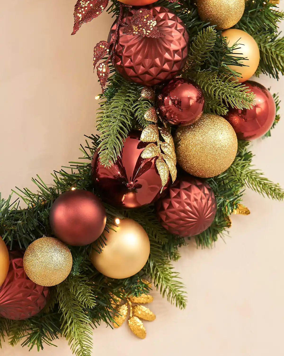 Side view of decorative wreath with red, gold, and green ornaments on a light background