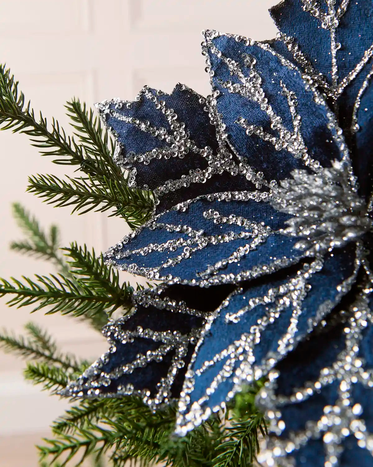 Side view of navy blue glitter poinsettia petals with silver embellishments on a Christmas tree