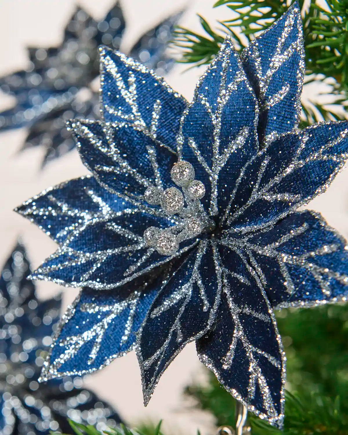 Side view of navy blue glitter poinsettia petals with silver embellishments on a Christmas tree
