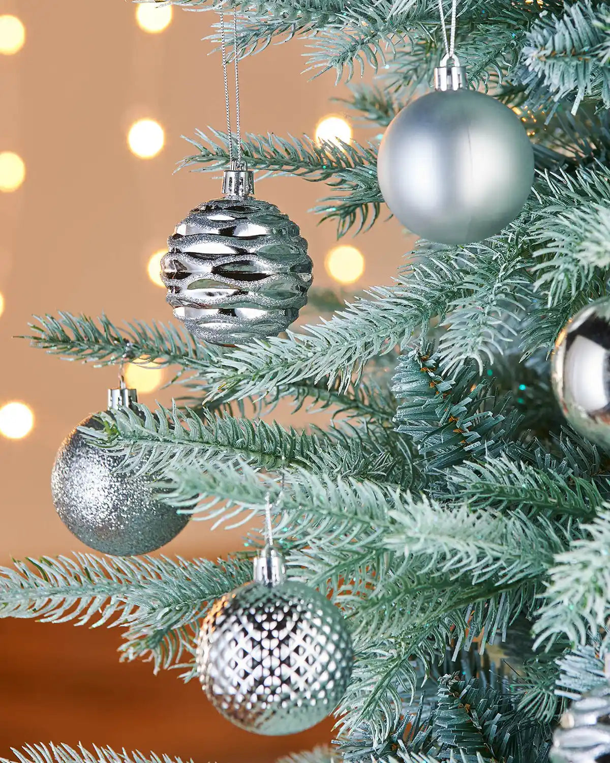 Silver Christmas baubles on a decorated tree with a warm glow in the background