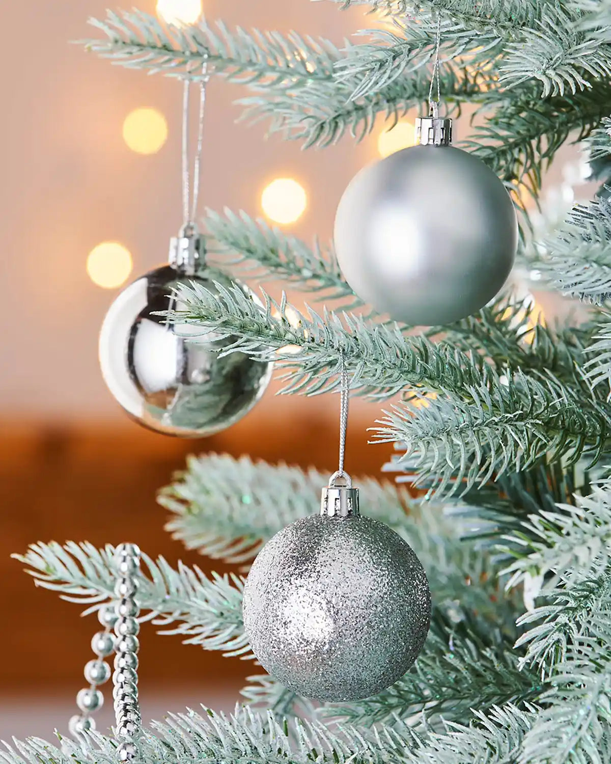 Silver Christmas baubles on a decorated tree with blurred lights in the background