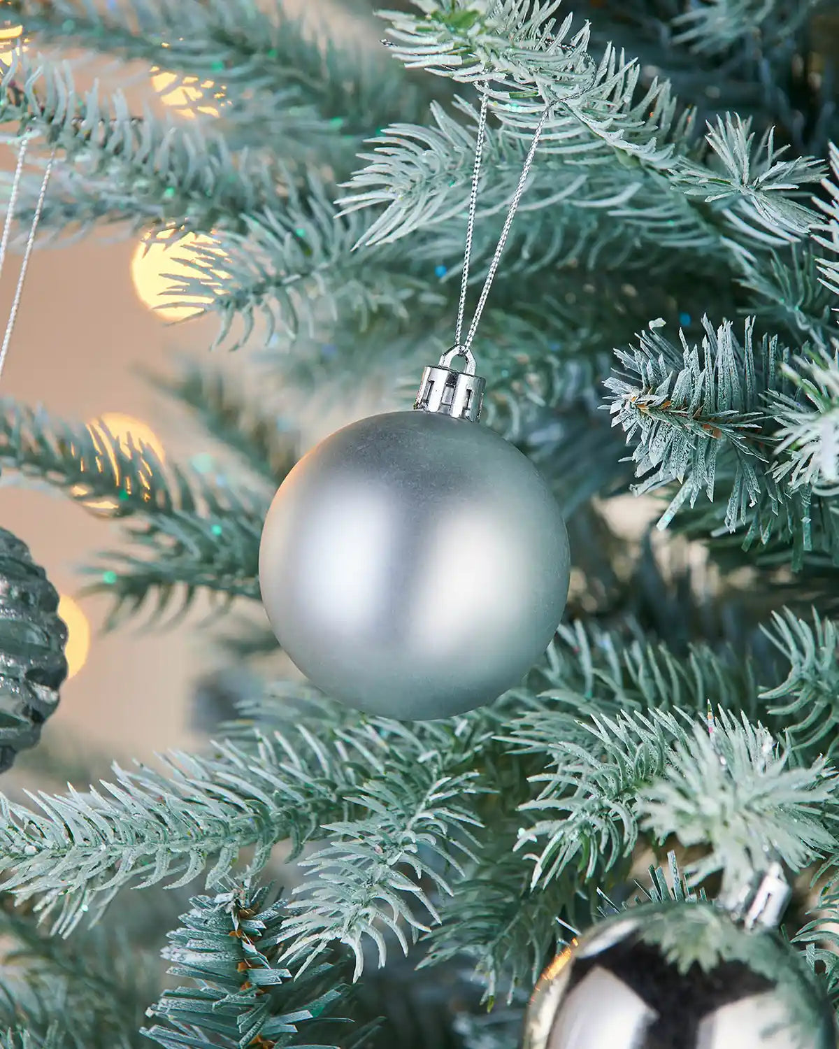 Silver Christmas matt bauble on a tree with blurred lights in the background