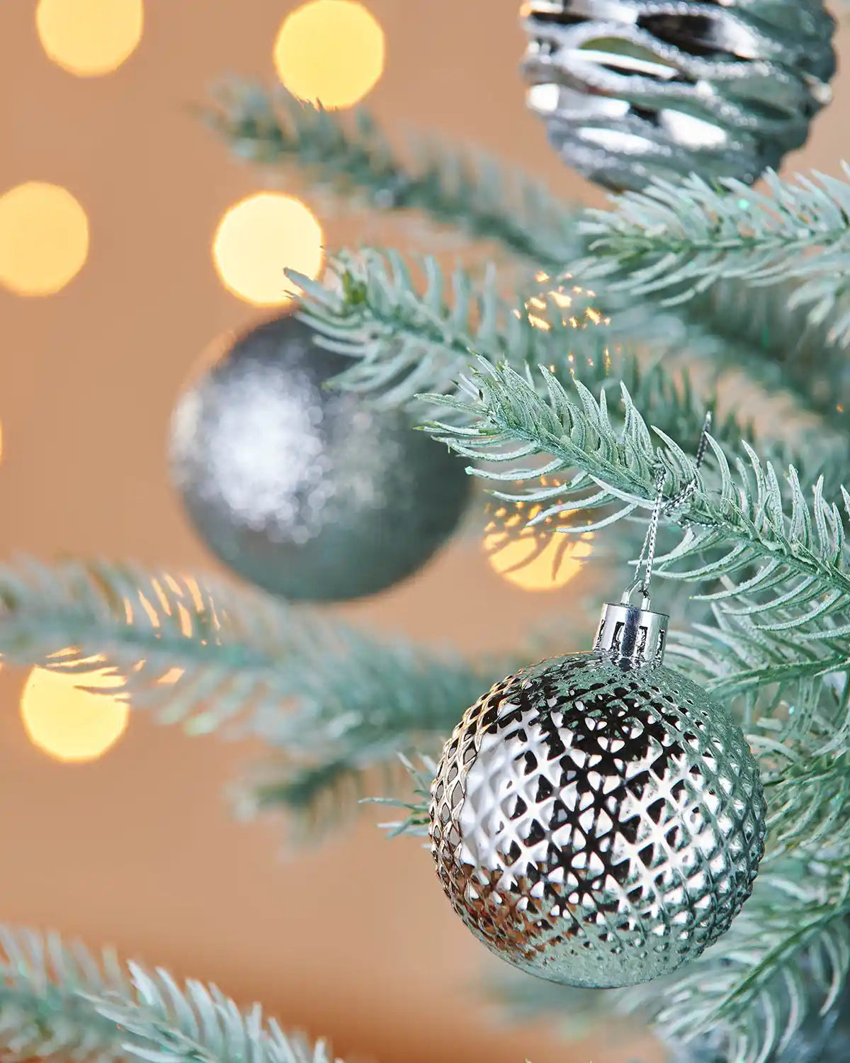 Silver Christmas textured bauble on a tree branch with blurred lights in the background