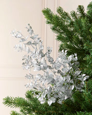 Silver Foliage Spray arranged among green Christmas Tree branches, showcasing its metallic Silver leaves and delicate stems.

